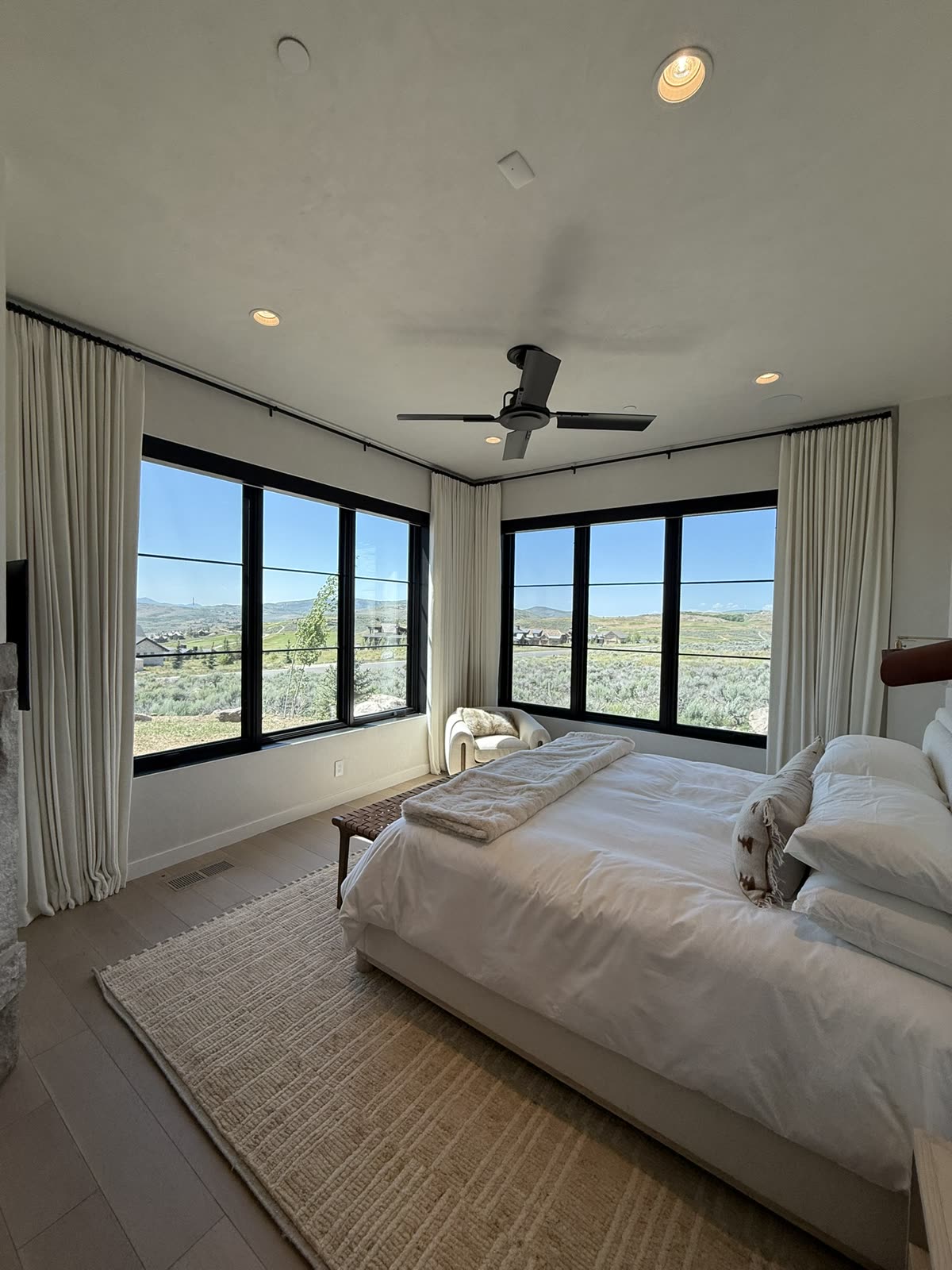 Floor-to-ceiling drapery on a black rod around corner windows in a bedroom, designed and installed by Blindznation